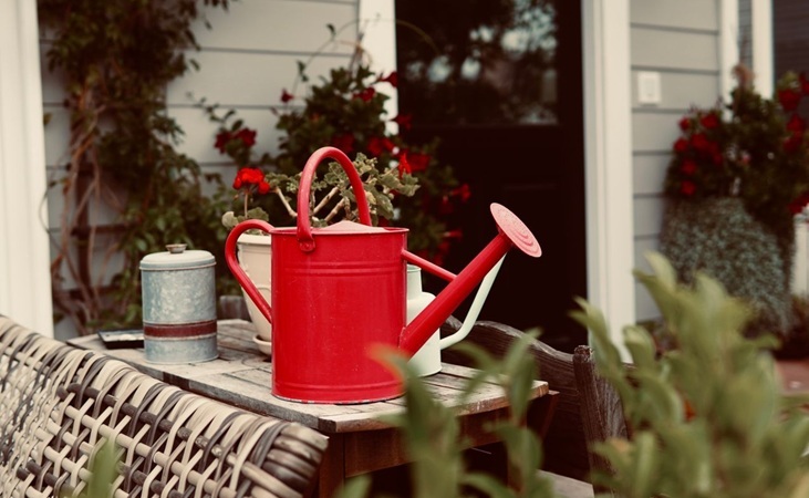 A red watering can on a table beside some containers A red watering can on a table beside some containers